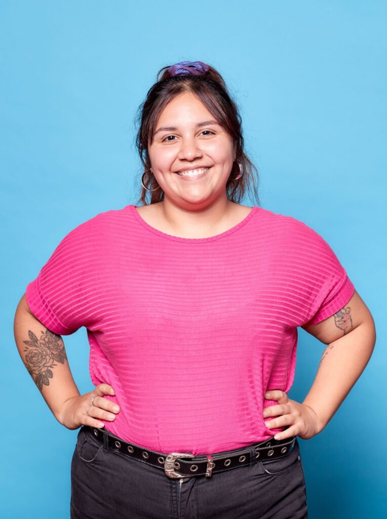 Image décorative d'une jeune femme tatouée portant un t-shirt rose sur un fond bleu clair.